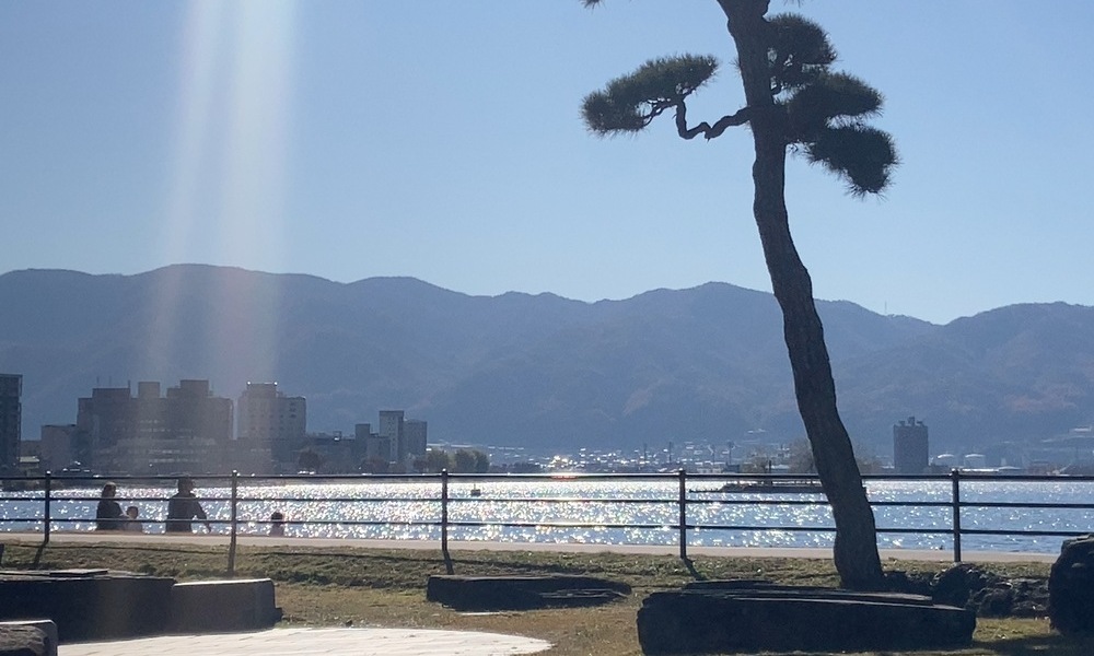 諏訪湖畔の足湯から眺めた湖と山並み、冬の光が水面に反射している風景