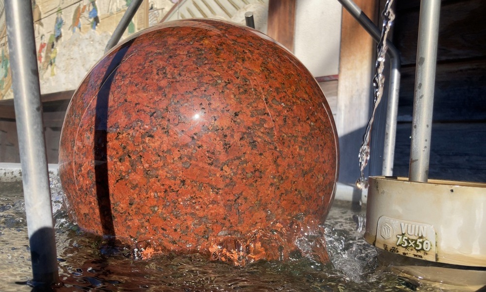 下諏訪宿問屋場跡・綿の湯跡で湧き出る温泉、石の球体の表面を水が静かに流れている様子