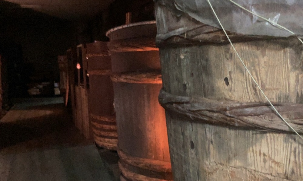 味噌蔵の内部に並ぶ木桶。暗い蔵の中で、長期間の発酵のために静かに置かれている。