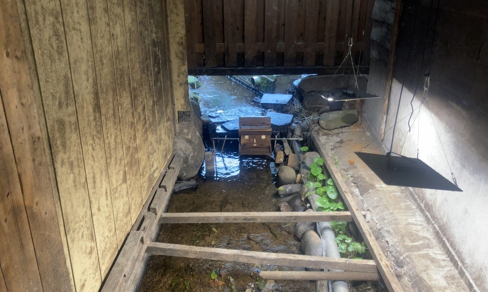 味噌蔵の床下に流れる水と石。木の床組みの下で、水が静かに溜まり、ゆっくりと流れている様子。