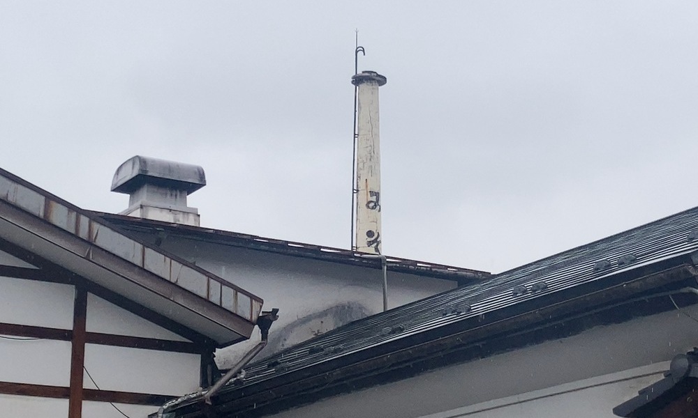 味噌蔵の屋根と煙突。低い建物の上に、一本の煙突が空に向かって立っている。