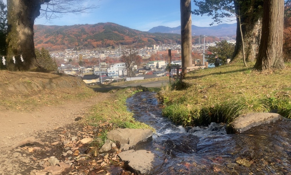 町へと流れ下る小さな水路と、その向こうに広がる盆地の風景