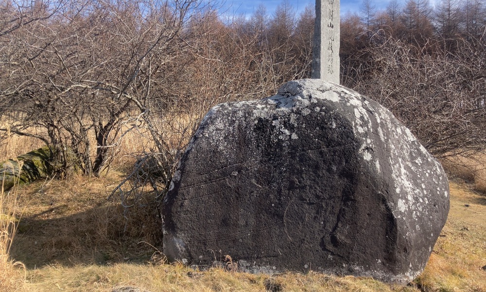 旧御射山に残る祭場跡の巨石と標柱。諏訪信仰の原型を伝えるとされる、草原に佇む黒い磐座