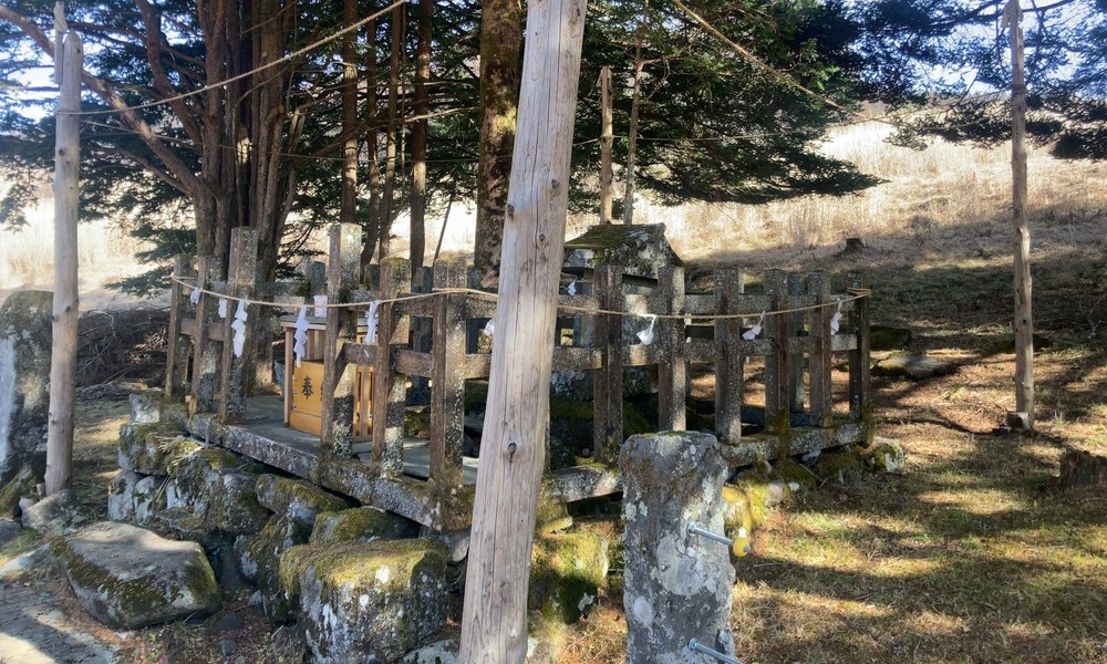 旧御射山の一角に残る石の祭祀基壇と木柵。注連縄が張られ、周囲を木立に囲まれた小さな祈りの区画