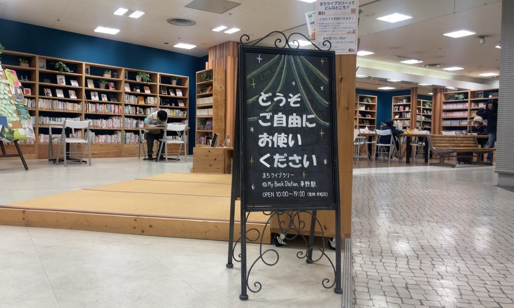 「どうぞご自由にお使いください」の看板越しに見える、まちライブラリーの閲覧スペース