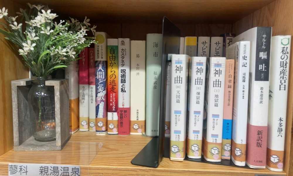 花と本が並ぶ、まちライブラリーの木製本棚の一角