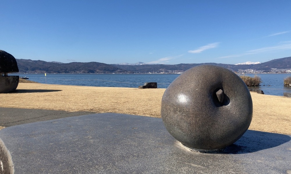 諏訪湖畔に設置された黒い石の球体と湖面