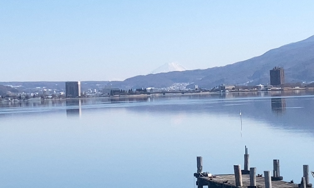 静かな諏訪湖の湖面と遠景にうっすら見える富士山