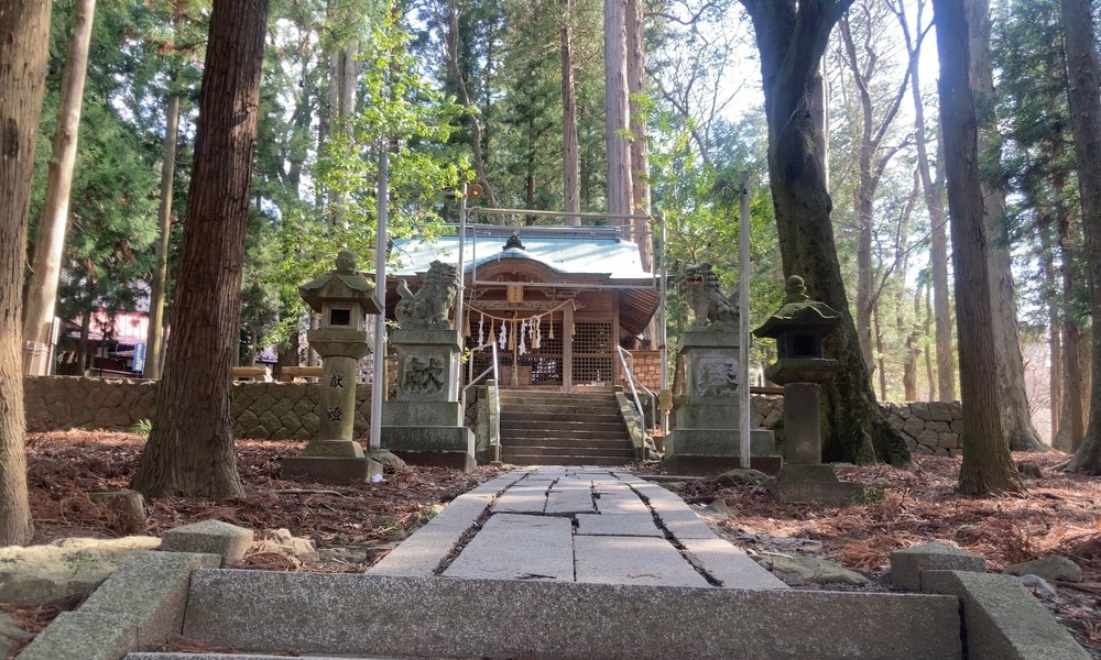 石畳の参道の先に小さな社殿が見え、森の静けさの中に神話の気配が残る境内風景