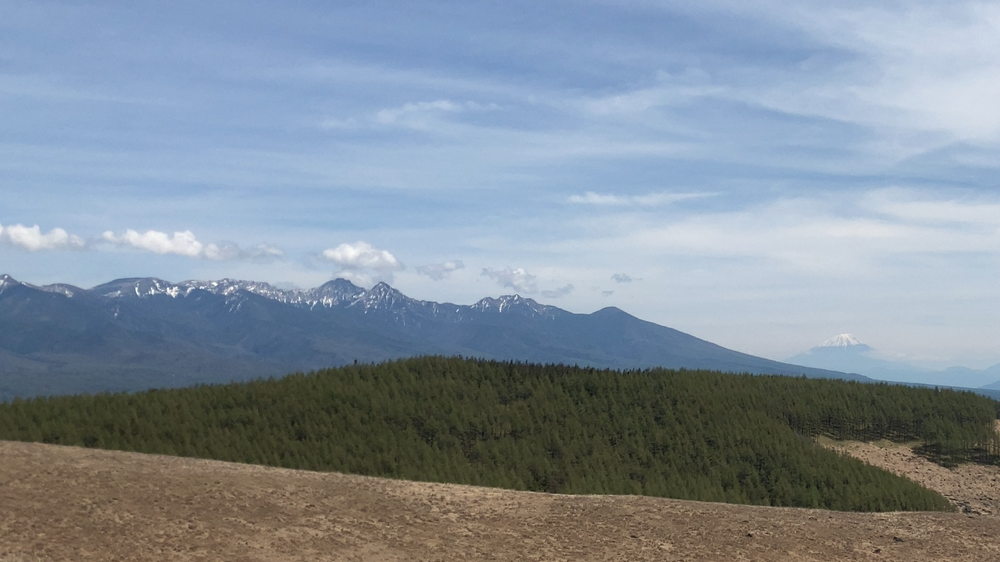 八ヶ岳の連なる稜線の奥に富士山が小さく見え、対比される二つの山の関係を静かに示す風景